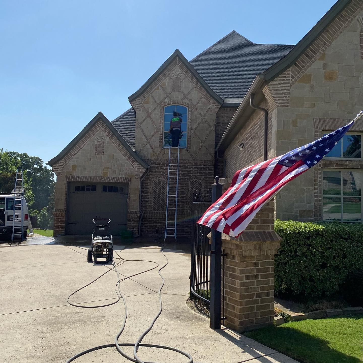 Man washing window on large brick home; American flag flies.