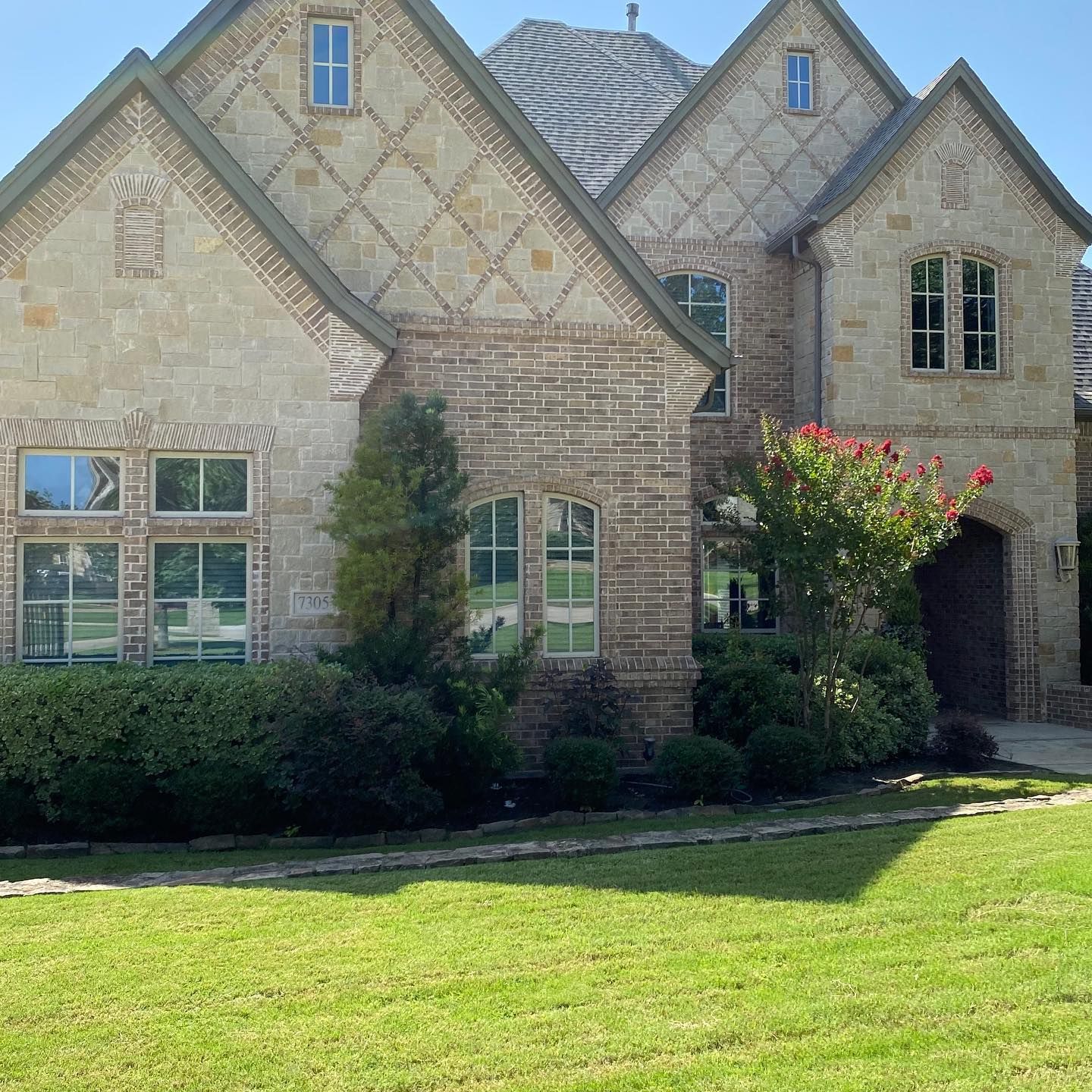 Tan stone house with green lawn and bushes; blue sky overhead.