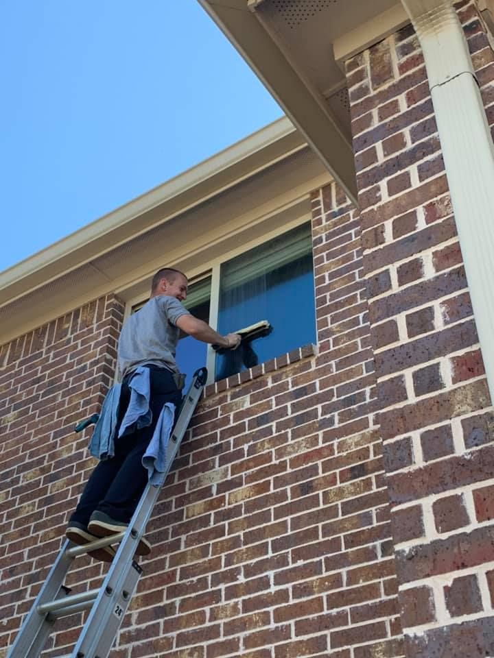 Man on ladder washing window on a brick house.