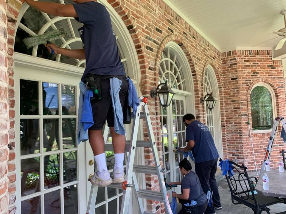 Window cleaners on ladders washing large windows on a brick building.