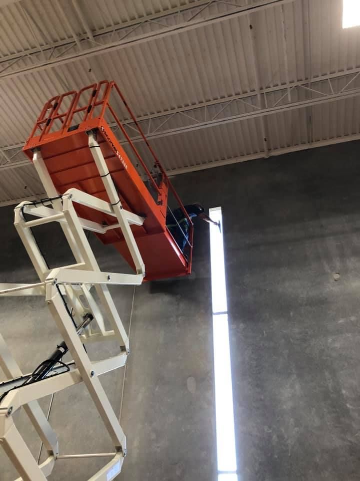 Orange scissor lift extending towards a ceiling. Person in basket near gray wall.