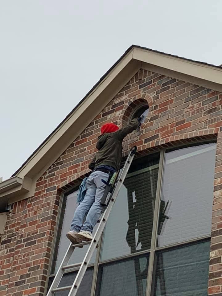 Man on ladder cleaning a window of a brick house, reaching for an arched opening.