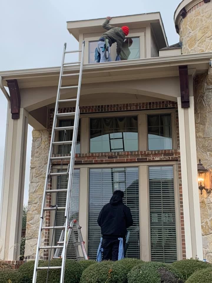 Window washers on a tall ladder cleaning windows of a house. One is at the top, two are working below.