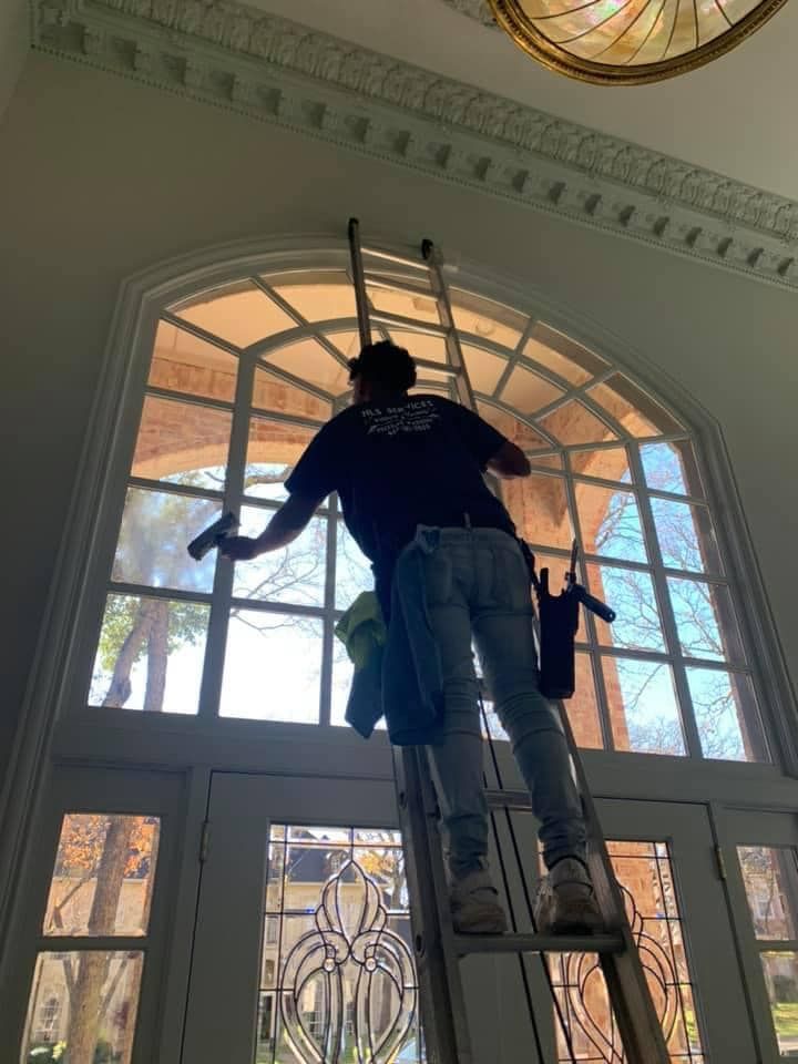 Person on a ladder cleaning a large arched window above double doors.