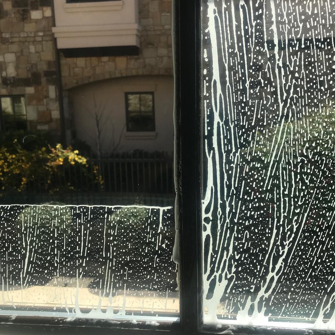 Window being cleaned, with streaks of soapy solution.  Exterior view shows building and foliage.