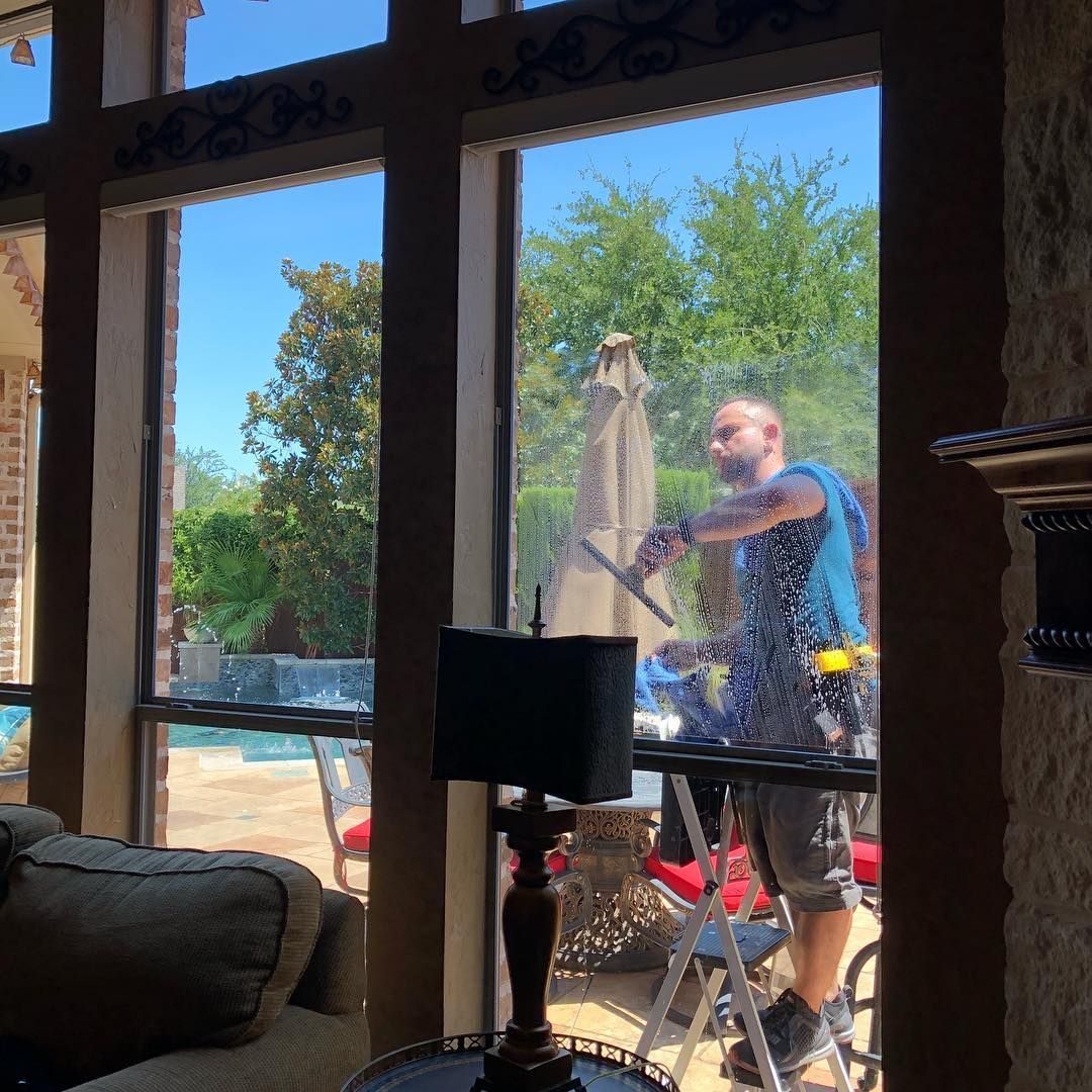 Man washing a window, using a squeegee. He's on a ladder, sunny outdoor view.