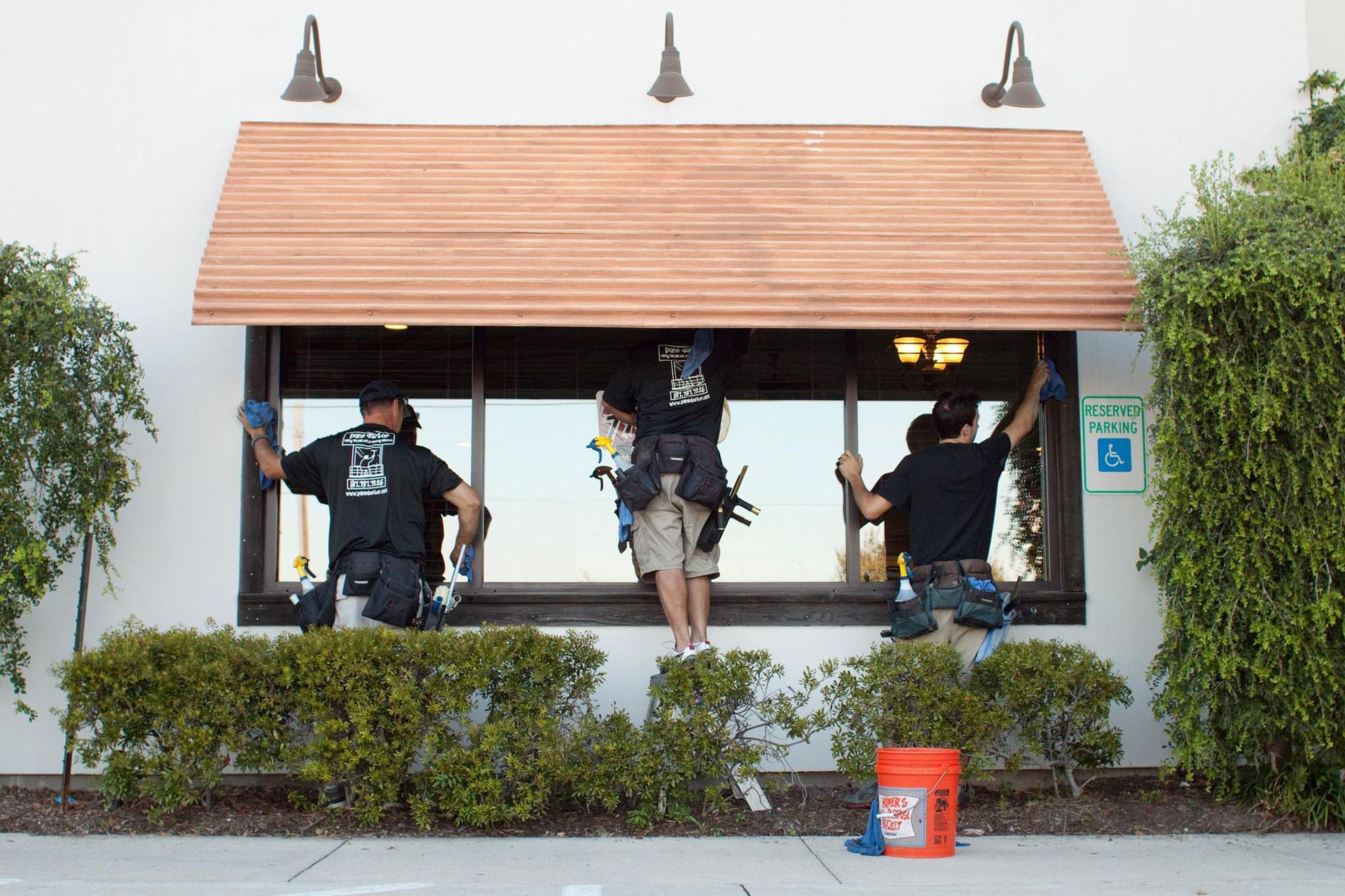Three window washers installing a wooden awning above a storefront window.