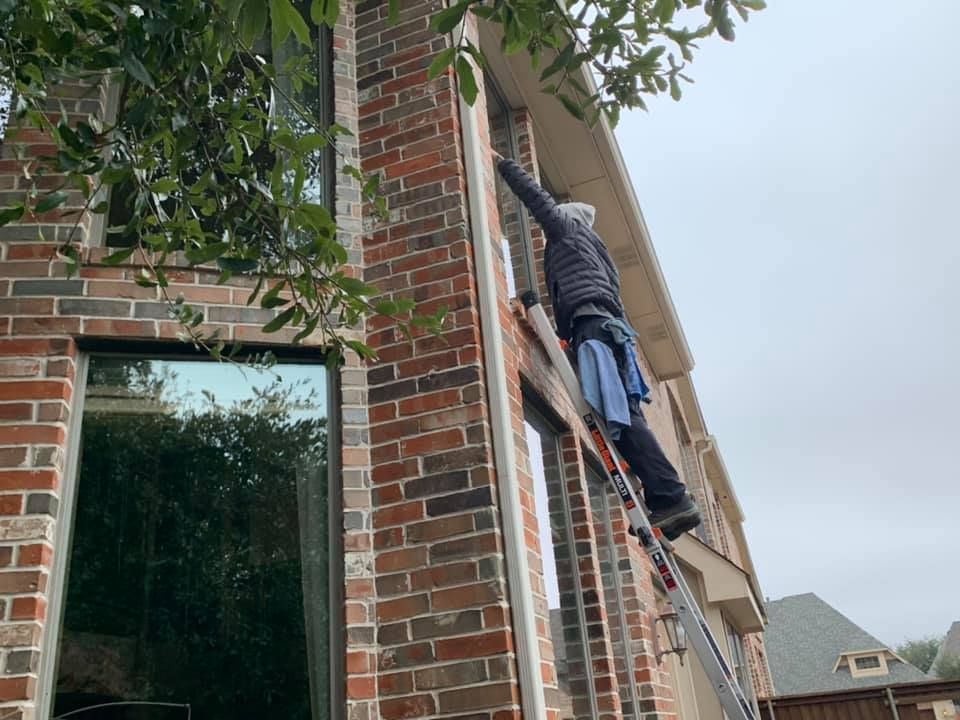 Person on ladder cleaning window of brick building, outdoors.