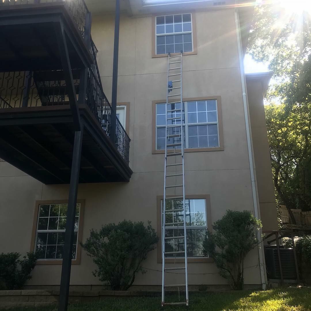A tall ladder leaning against a two-story building with windows.