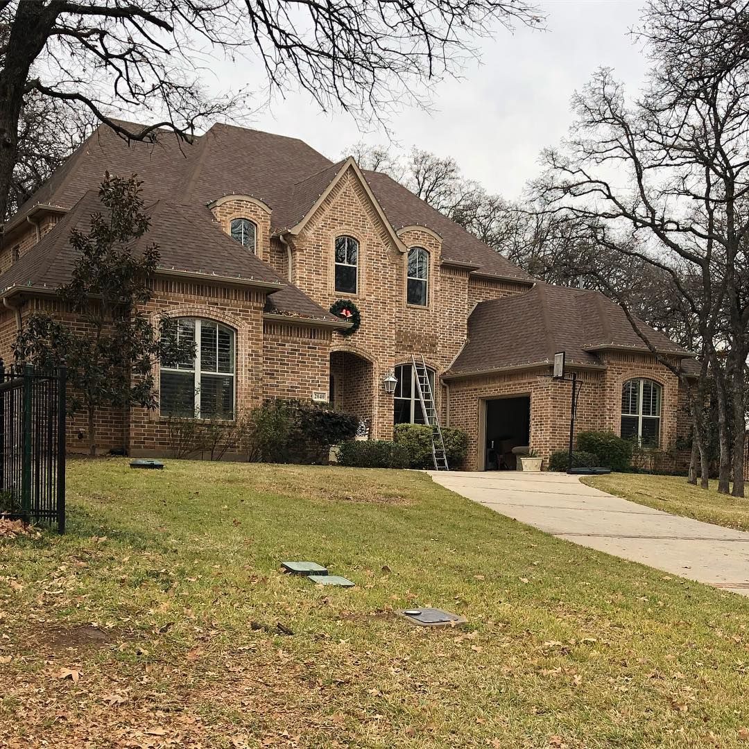 Brick house with brown roof, windows, and driveway on a grassy yard with bare trees.