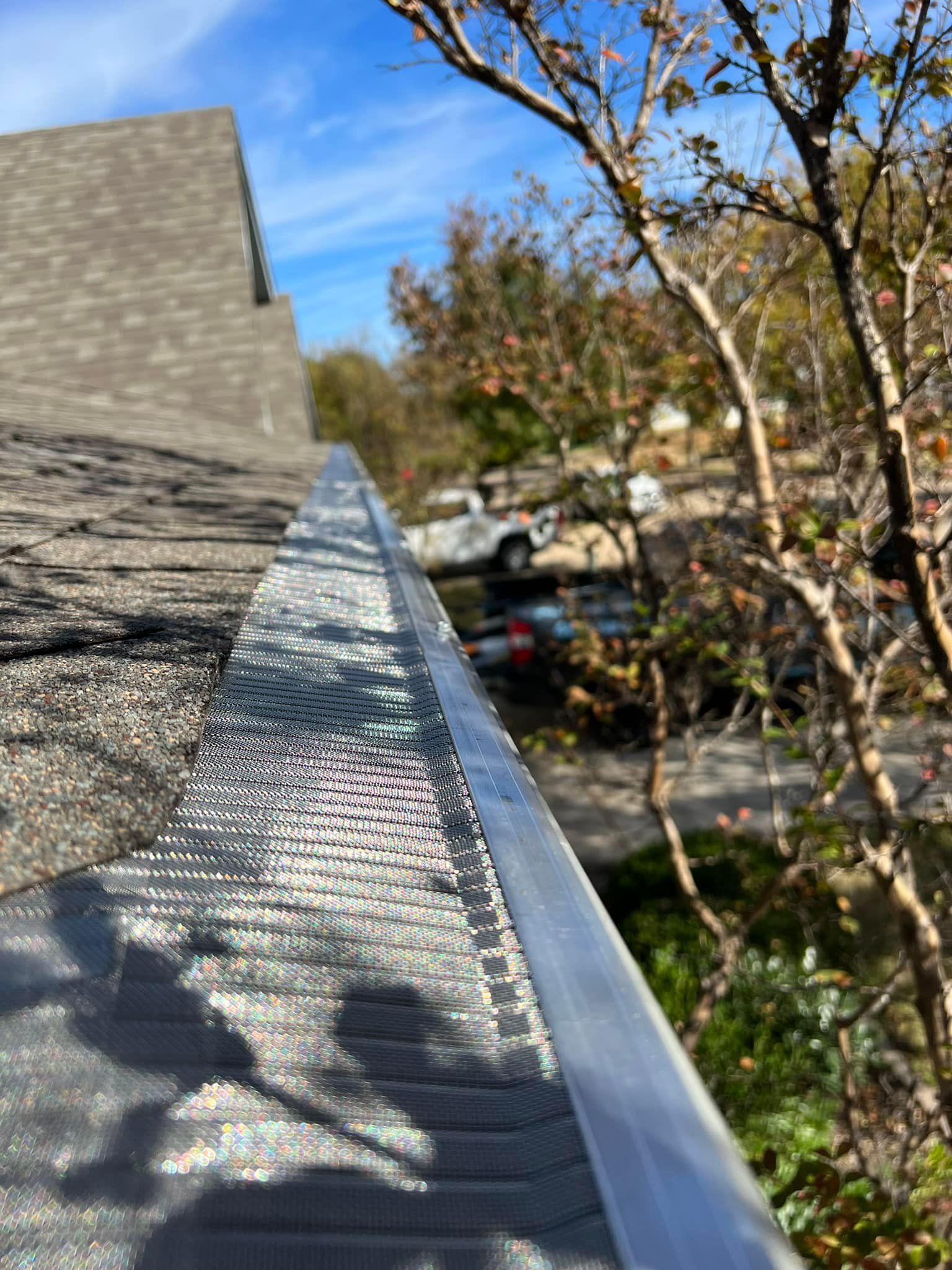 Gutter filled with debris on a roof, a white truck and fall foliage in the background.