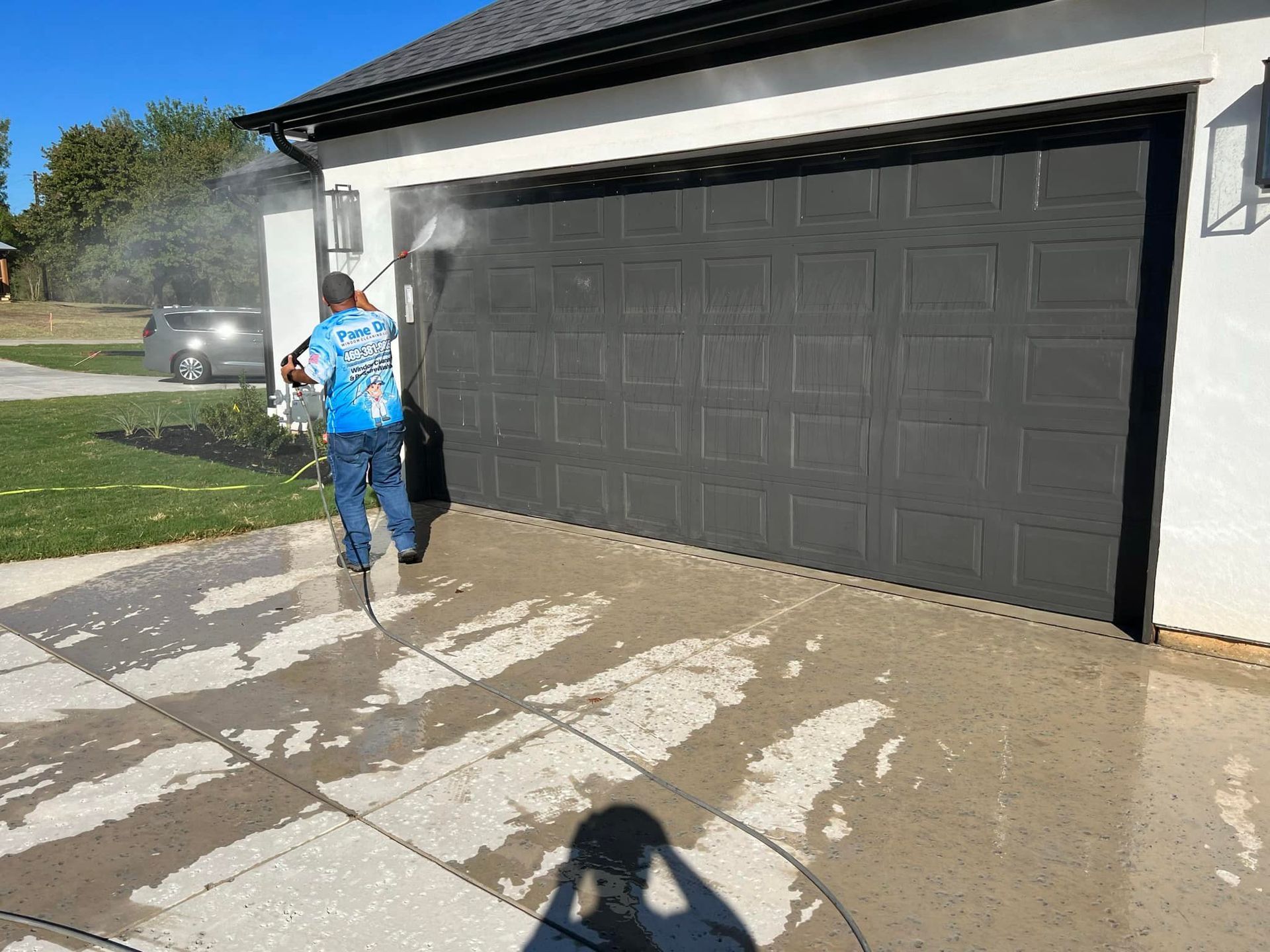 Person pressure washing a dark gray garage door and concrete driveway.