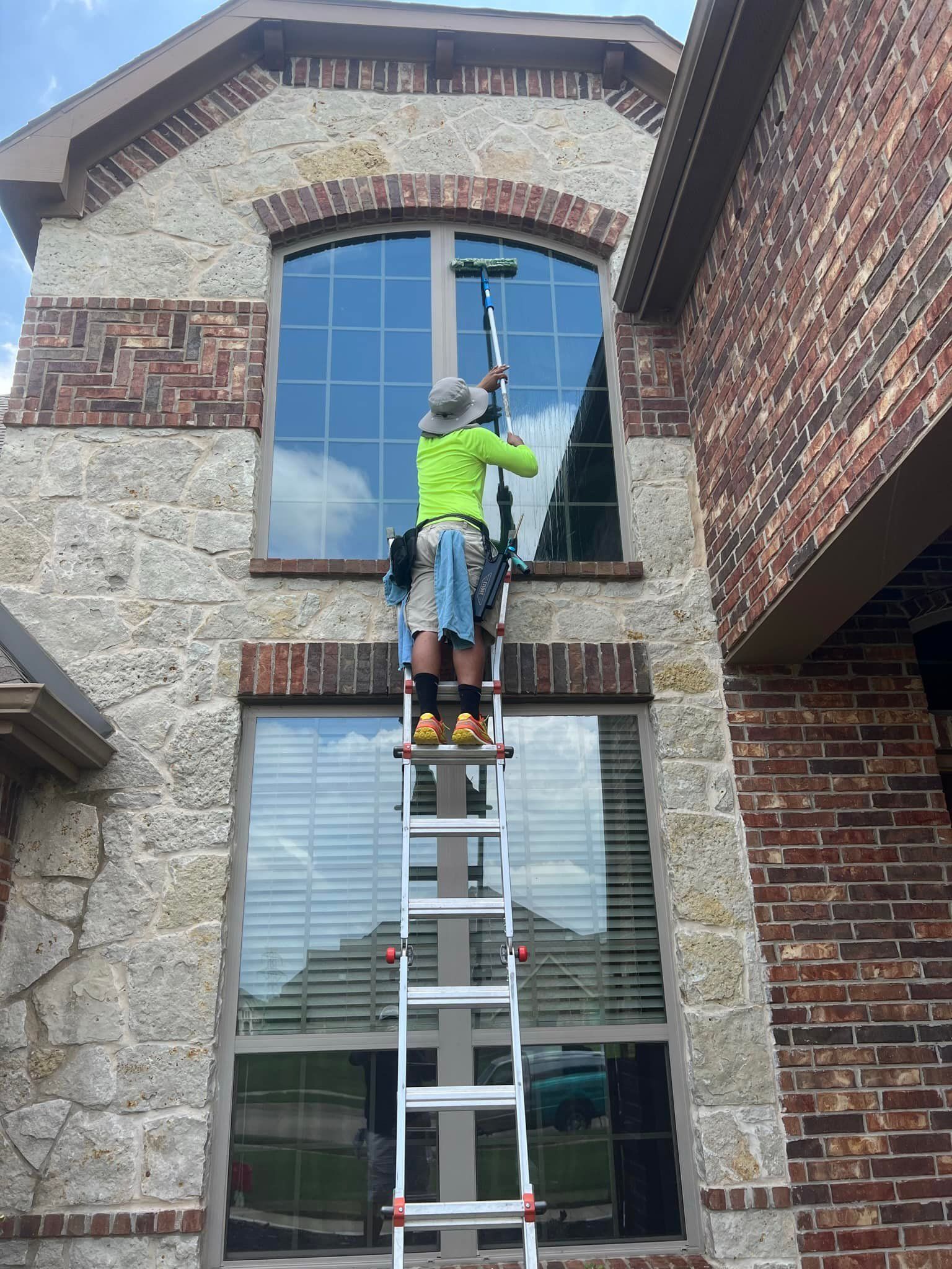 Person cleaning a large window on a building, using a ladder and squeegee.