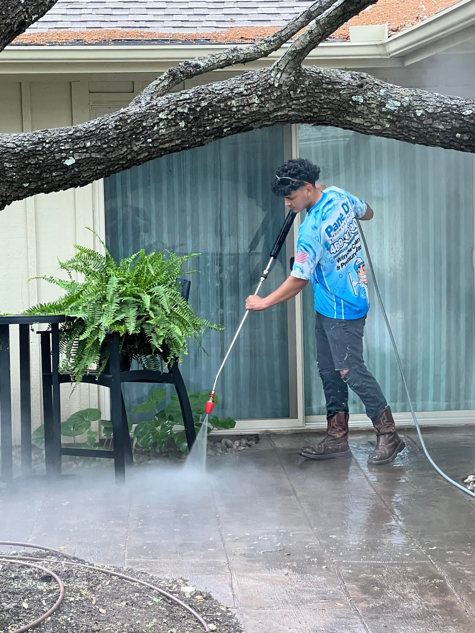Young man power washing a patio. Overhanging tree branch.