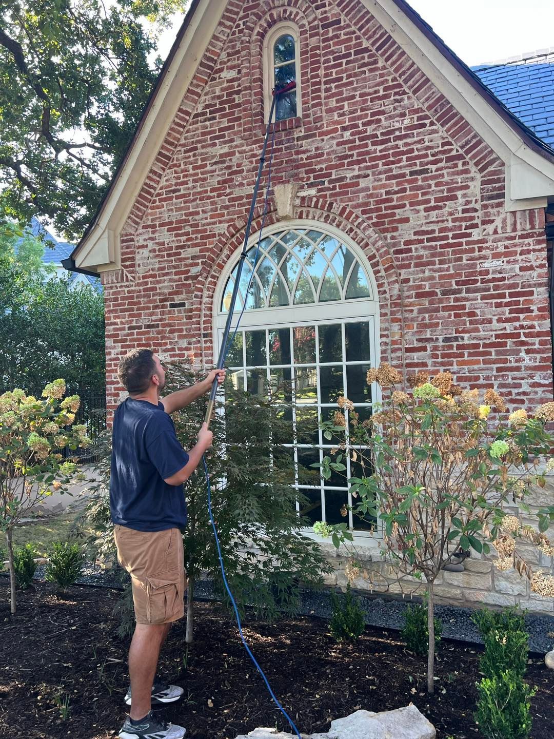Man cleaning window on brick house with long tool.