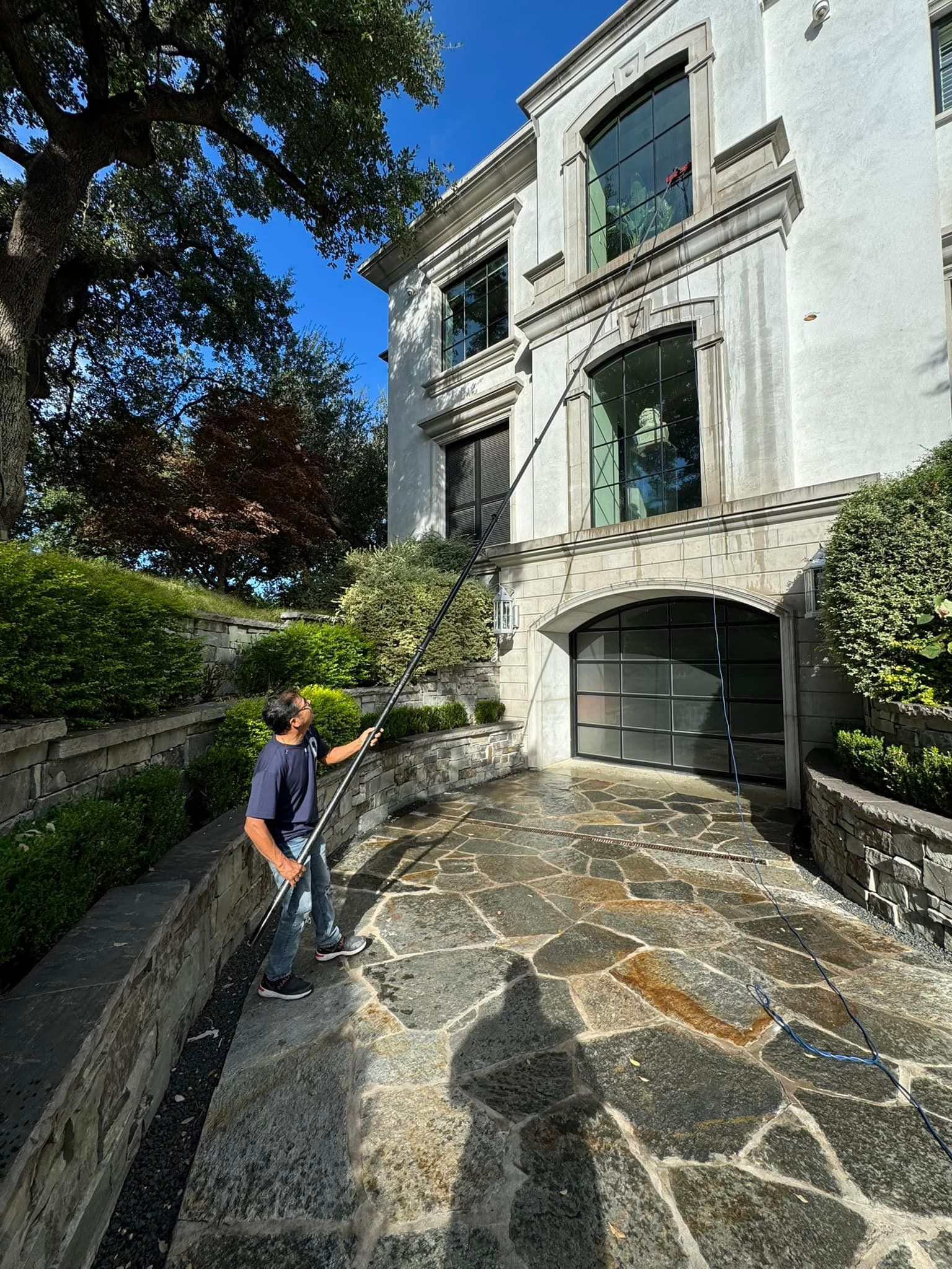 Person washing windows of a large white house with a long-handled brush on a sunny day.