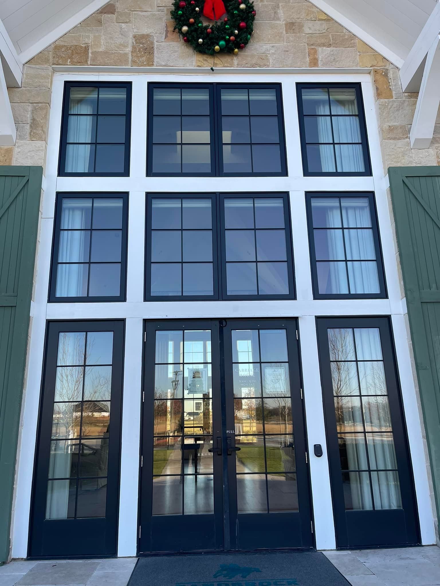 Black-framed windows and doors on a building's facade, with a Christmas wreath above.