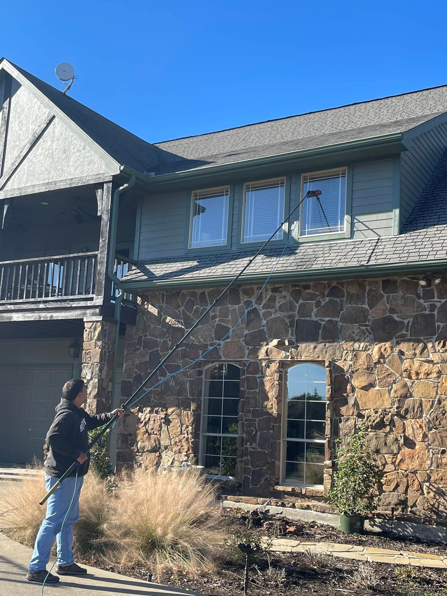 Person washing windows of a two-story house with a long-handled brush on a sunny day.