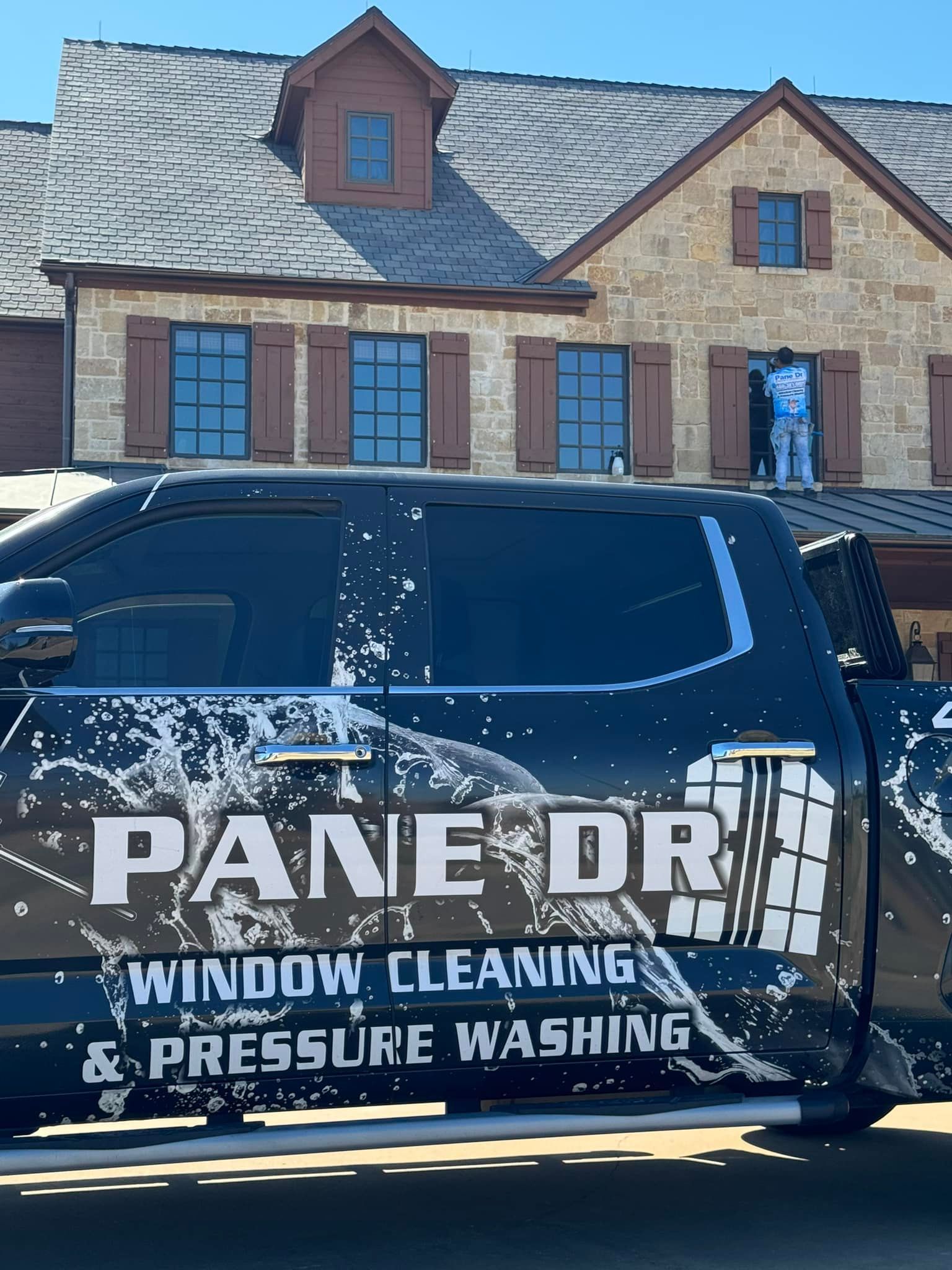 Window cleaning truck with logo in front of a house, worker on the roof, blue uniform.