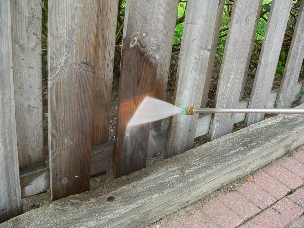 A power washer spraying a wooden fence, cleaning away grime and discoloration.