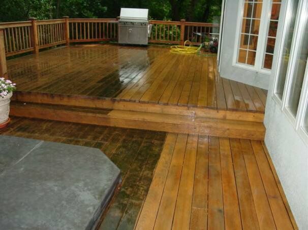 Wooden deck, possibly wet, with steps leading to a railing. A grill and hose are visible.