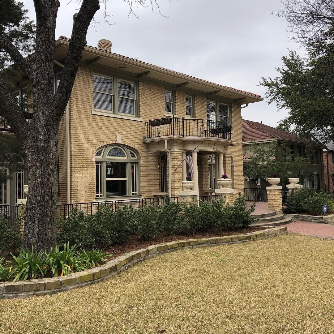 Two-story beige brick house with a small balcony and stone trim on a cloudy day.