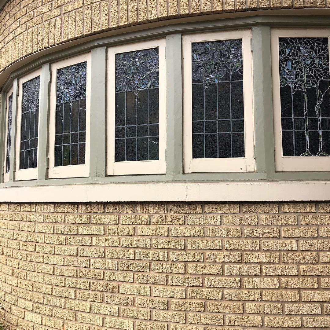 Curved brick wall with light green-framed windows featuring stained glass patterns.