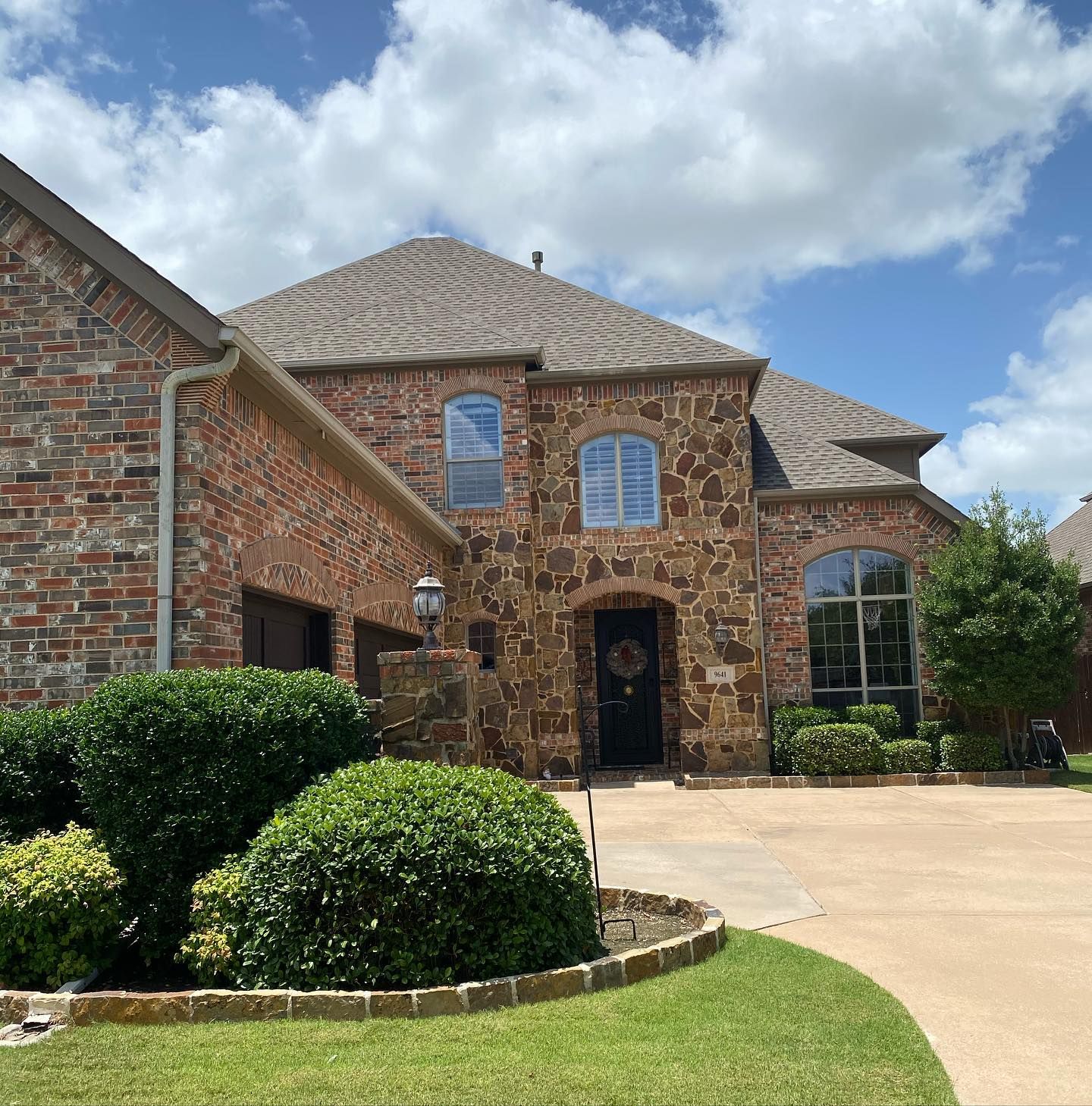 Two-story brick and stone house with a dark door and arched windows on a sunny day.