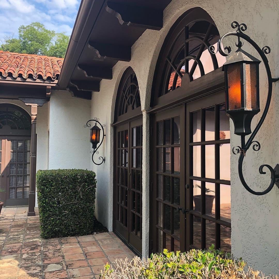 Spanish-style building with arched doors, iron sconces, red tile roof, white stucco walls.