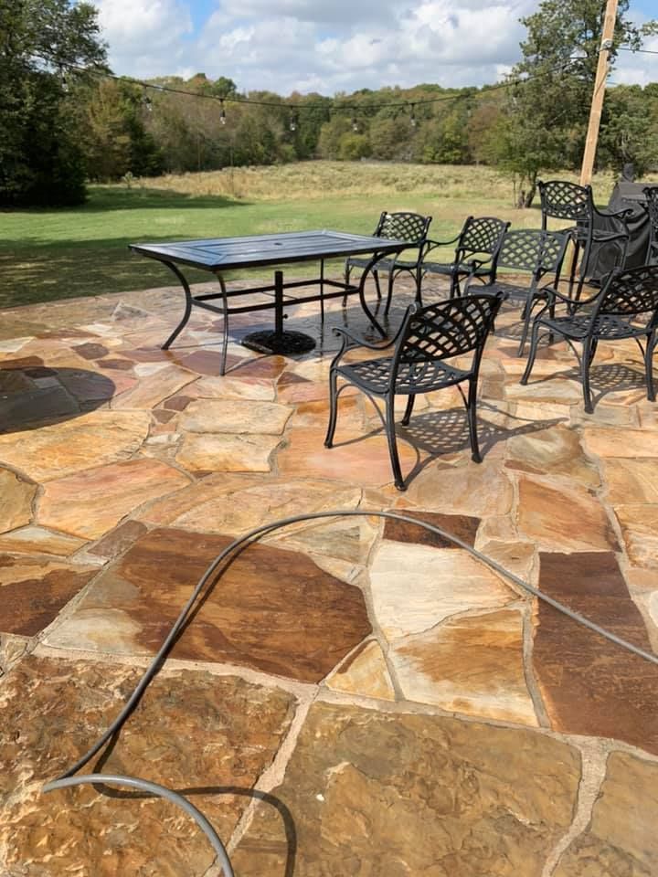 Patio with stone floor, black table and chairs, green field in the background.