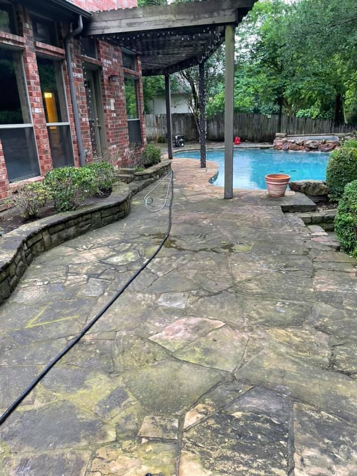 Flagstone patio with pool in the background, a brick house on the left, and a pergola overhead.