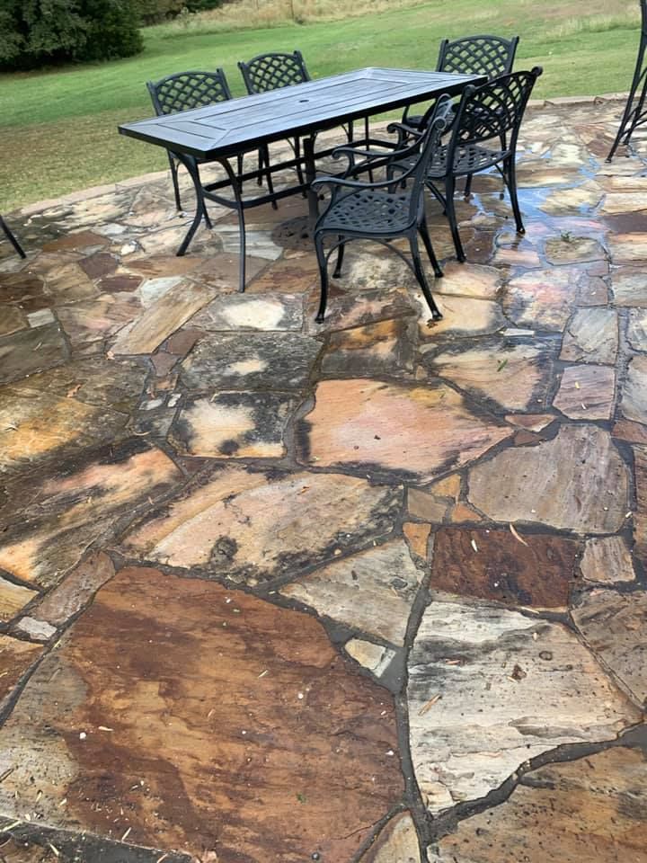 Patio with flagstone flooring, dark table and chairs on a wet day, green lawn in the background.