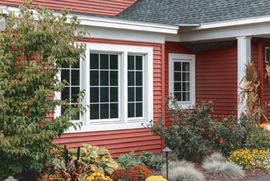 Red house with white trim and multiple windows, surrounded by landscaping.