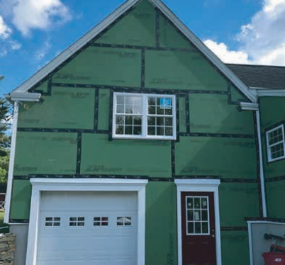 Green house exterior with white window, garage door, and door; blue sky.