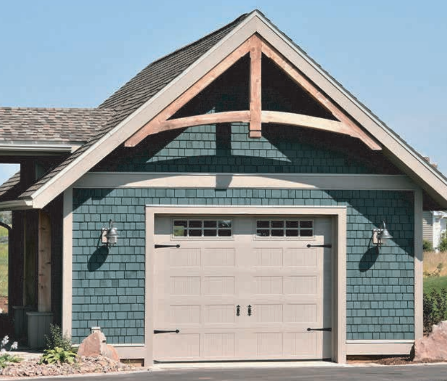 Blue-shingled garage with tan door, accented with wood trim, under a gabled roof with decorative timber.