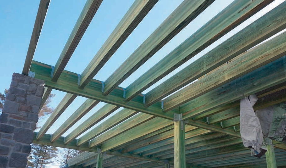 Wooden pergola frame under a bright blue sky. Green-treated wood is exposed.