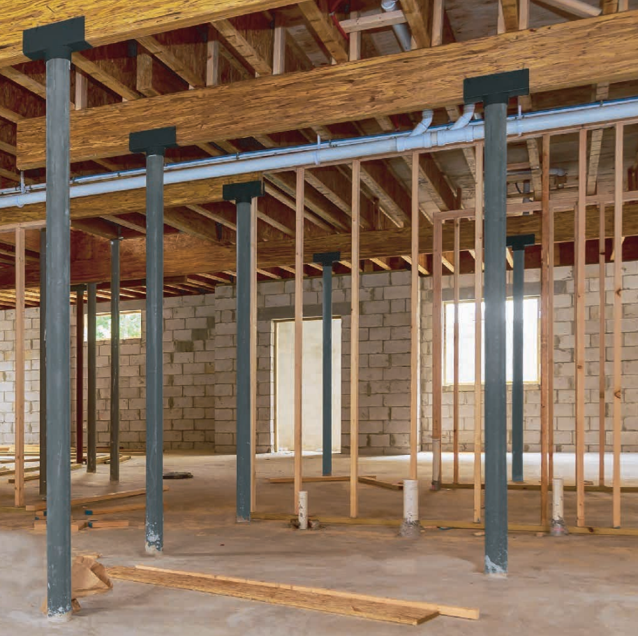 Interior view of a basement under construction with concrete block walls, wooden framing, and support columns.