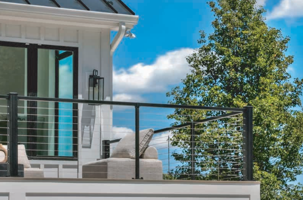 Deck with modern cable railing, white siding, and blue sky.