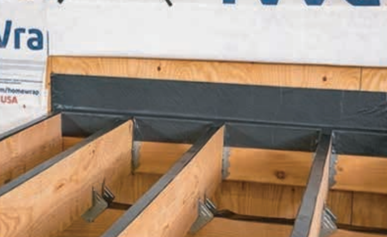 Black flashing installed on a wood deck frame, above the joists and against a wall.