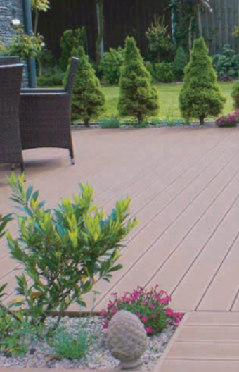 A brown deck with a small bush and a stone in a garden, with cone-shaped trees in the background.