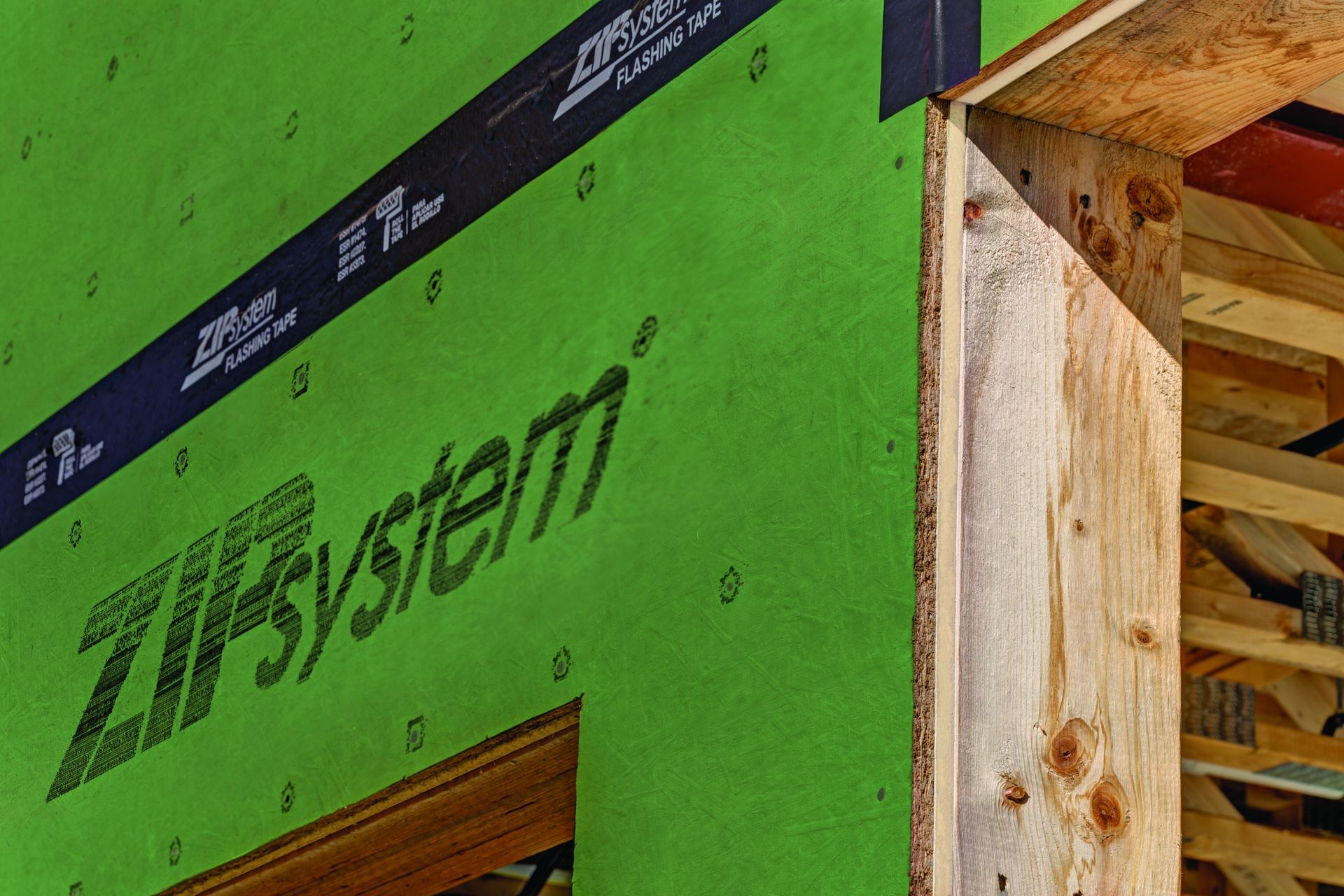 Green ZIP System sheathing on a building frame; black tape seals edges.