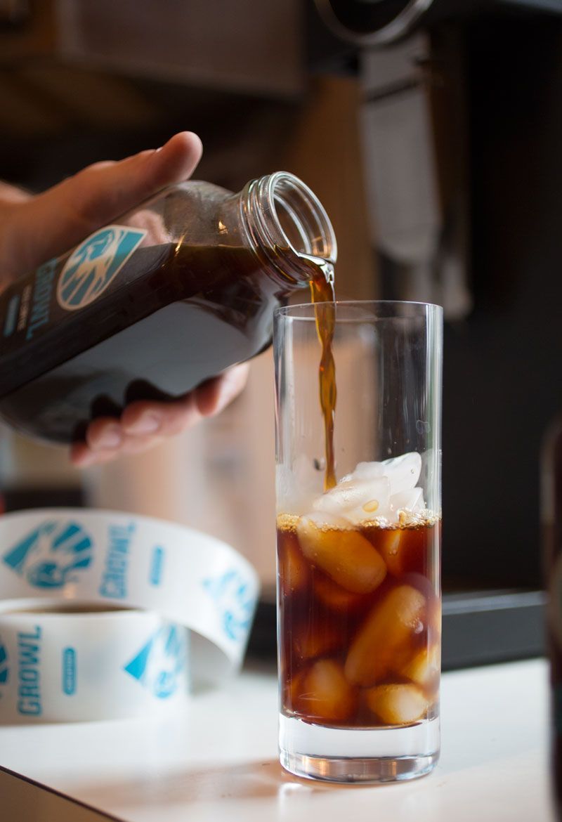 A person pouring a drink into a glass with ice cubes