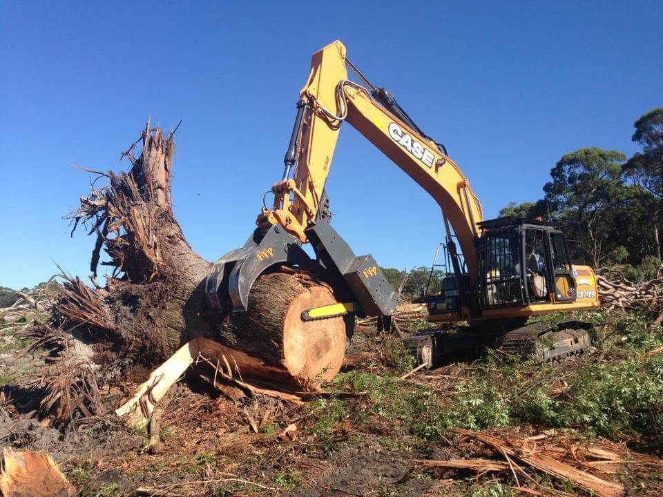 A large excavator is moving a large log in a field.