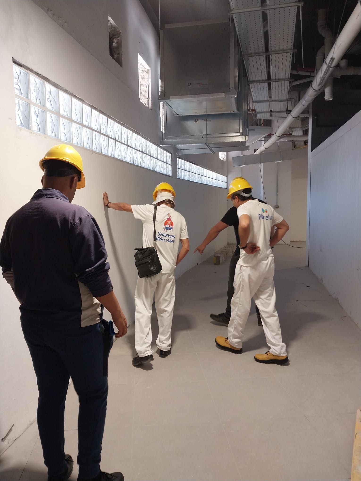 Un grupo de trabajadores de la construcción está de pie en un pasillo mirando una pared.