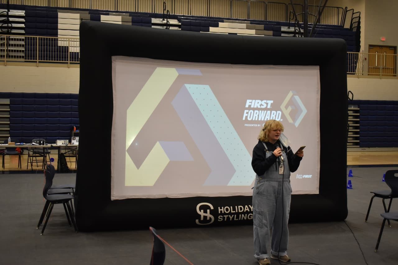 Student speaking at event with inflatable screen. Gymnasium setting.
