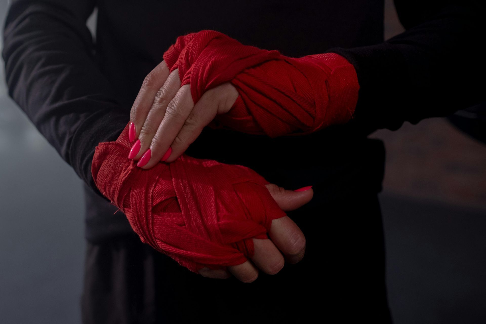 Person in black clothing wrapping red hand wraps on their wrist.