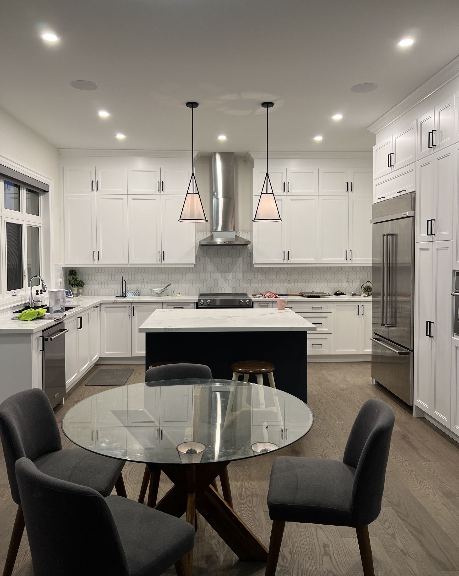 A kitchen with white cabinets , stainless steel appliances , a glass table and chairs.