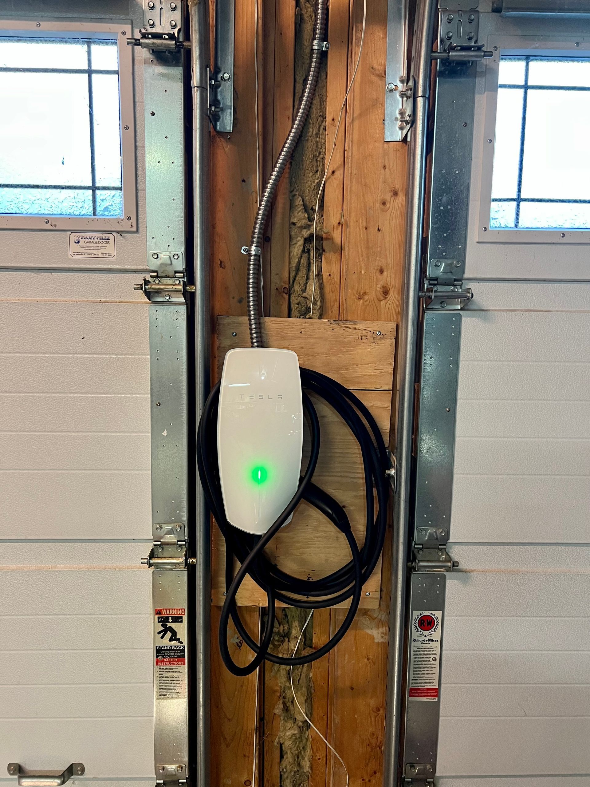A tesla charging station is attached to the side of a garage door.