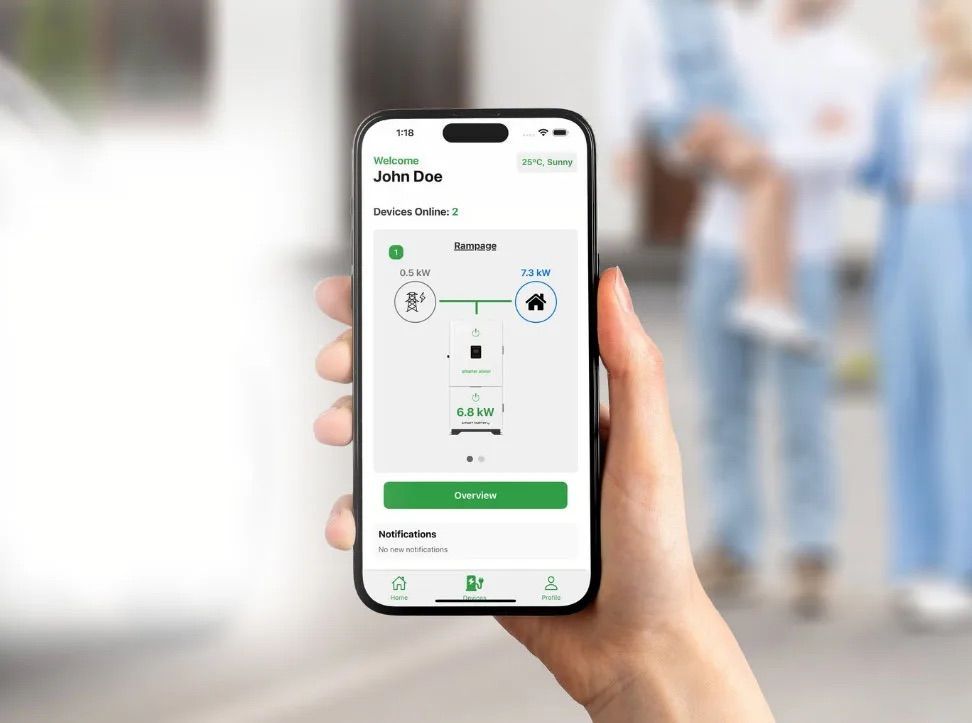 A hand holding a smartphone displaying a smart home app interface; family blurred in background.