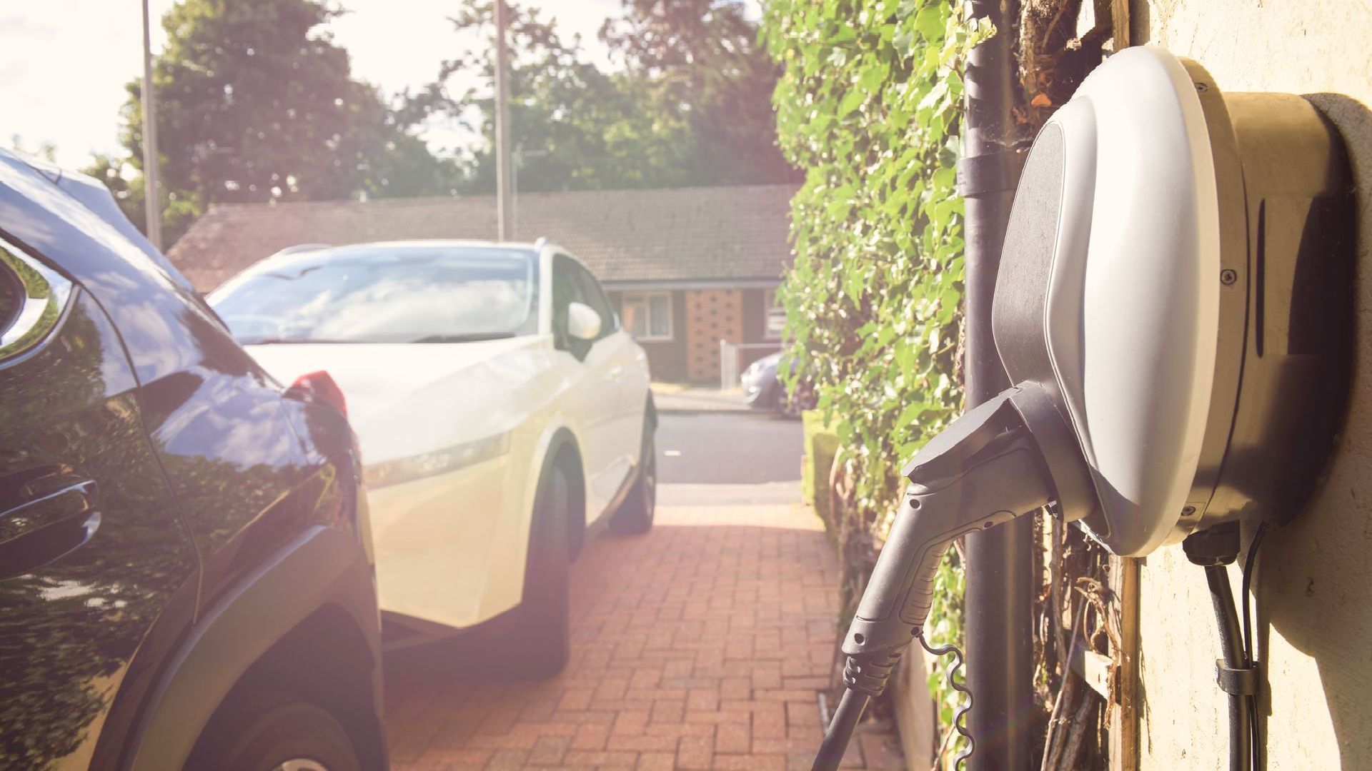 Two cars are parked in a driveway next to a charging station.